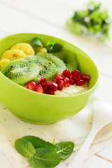 Healthy breakfast: fresh cottage cheese with kiwi, banana, garnet seeds and honey decorated mint leaves on white wooden table. Selective focus