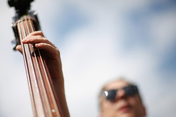 Hand virtuoso musician on contrabass fretboard on a background cloudy sky