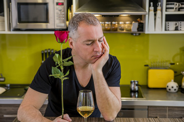 Fototapeta na wymiar Attractive man with flowers in his hand is waiting. The thoughtful man in kitchen, waits for the woman