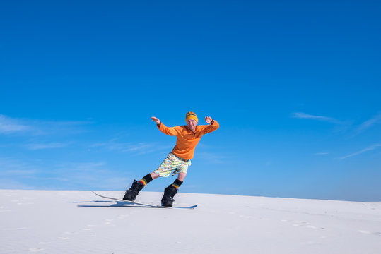 Joyful man rides on the snowboard in desert