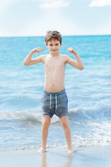 Fototapeta na wymiar Happy 7 years boy in victory success gesture on the beach.
