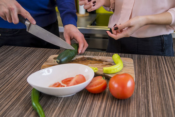 couple preparing vegetables together at home in the kitchen. Closeup of human hands cooking vegetables salad in kitchen on the wooden table. Healthy meal and vegetarian concept