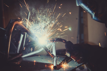 Worker with protective mask welding metal and producing smoke and sparks