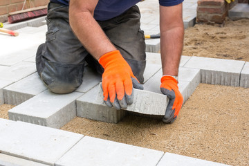 Hands of a builder laying new paving stones.