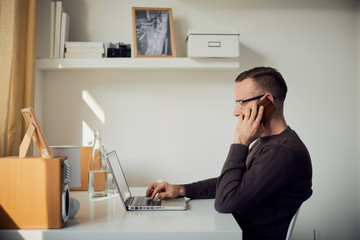 young man using phone and laptop, working as freelancer - obrazy, fototapety, plakaty
