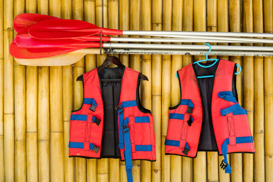 Red Life Jacket And Oars On A Wall Of Bamboo.