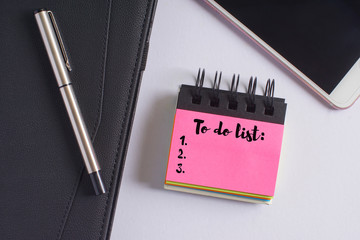 "To do list" words on pink sticky notes with fountain pen, diary and smartphone on white background - business and finance concept