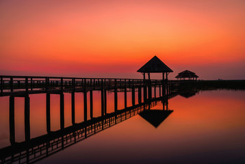 Fototapeta na wymiar Silhouette old wooden bridge and pavilion in lake at sunset