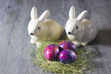 Easter decoration rabbits and eggs on a hay on a gray wooden background