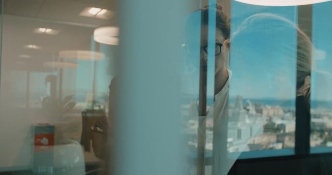 Business women having a meeting in modern office, standing in front of glass wall with post it notes, using digital tablet.