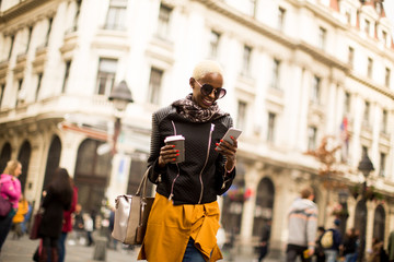 Beautiful stylish african american  woman holding coffee and using a smart phone