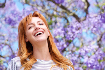Naklejka premium attractive young woman laughing by tree with purple flowers