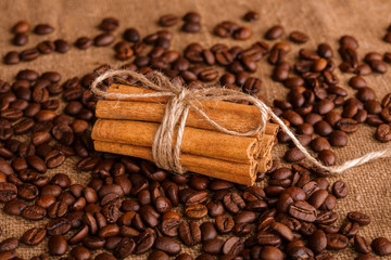 Coffee beans and cinnamon on a background of burlap. Roasted coffee beans background close up. Coffee beans pile from top with copy space for text. Seasoning. Spice. Cinnamon. Badian. Coffee house.