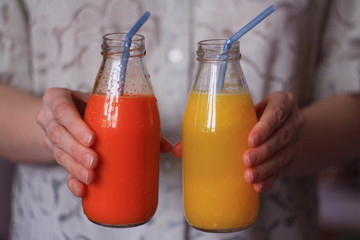 women's hands holding bottles with fresh carrot and orange juice