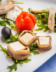 Appetizer from cheese, fish, herring, olive and tomato