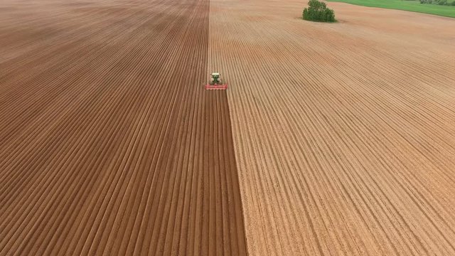 Aerial view of ploughed field with tractor sowing seeds of wheat. Industrial background on agricultural theme.Farm tractor and seeder planting crops on a field.Farm tractor handles field.