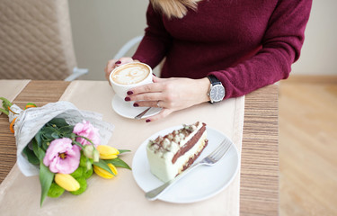 A pretty girl is sitting and waiting for someone. She is drinking some coffe or tea and eating croissants or some bakery cakes