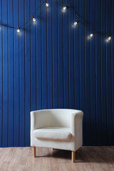 White fabric armchair on a background of blue wall with retro garland of light bulbs. Texture for the design