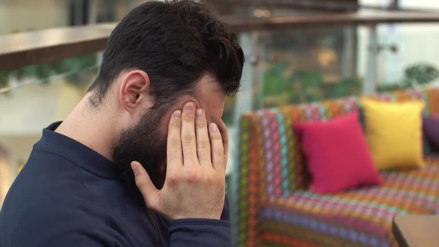 Young man with a big headache. He sits in a chair at the shopping mall