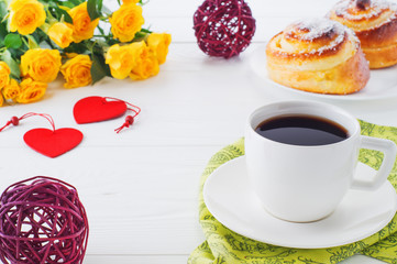 Cup of coffee with bouquet of yellow roses with copy space, close-up. Two spiral tasty buns with coconut chips, cup of black coffee and bouquet of roses. Delicious breakfast, sweet rolls and coffee. 
