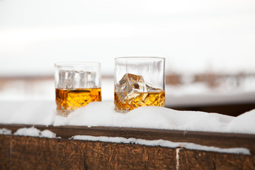 Two whiskey glasses in the snow on a winter background.