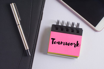 "Teamwork" words on pink sticky notes with fountain pen, diary and smartphone on white background - business and finance concept
