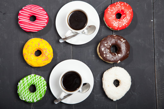 Colorful donuts and two cups of coffe on a black table