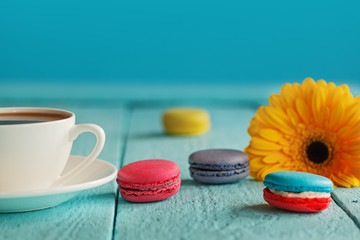Cup of coffee or tea with yellow flower and macaroons on blue background