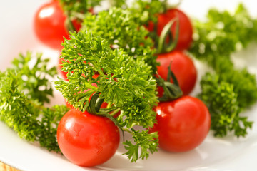 Fototapeta na wymiar Cherry tomatoes with curled parsley in white plate close up
