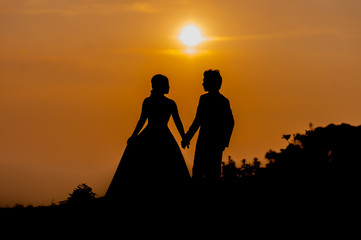 Obraz premium Silhouette of Asian Bride and Groom Standing on Mountain at Sunset