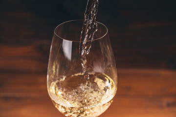 Pouring white wine from a bottle in a close up view of the wineglasses against wooden background