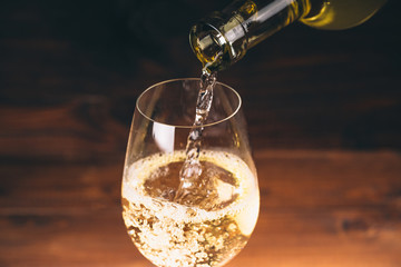 Pouring white wine from a bottle in a close up view of the wineglasses against wooden background
