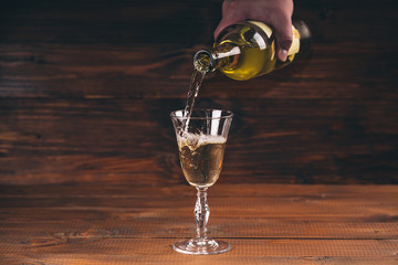 Pouring white wine from a bottle in a close up view of the wineglasses against wooden background