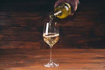 Pouring white wine from a bottle in a close up view of the wineglasses against wooden background