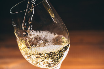 Pouring white wine from a bottle in a close up view of the wineglasses against wooden background