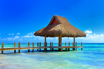 Tropical white sandy beach. Palm leaf roofed wooden pier with gazebo on the beach. Punta Cana, Dominican Republic