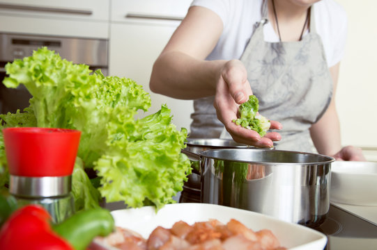 Woman puts vegetables into the pot. Conception of healthy food preparing.