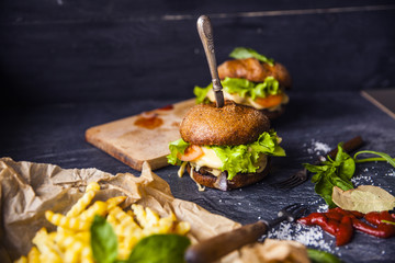 Fast food on the table: burger with beef or pork, or chicken and vegetables, French fries with tomato sauce, basil leaves