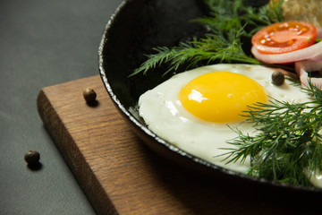 Fried eggs with potato pancakes and herbs in a pan on a black background. Homemade food.