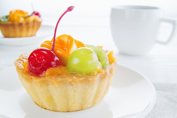 Appetizing cake basket with sliced fruit, berries and cup of coffee, on white background. Delicious and fresh dessert and coffee.  Morning choice.