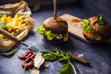 Fast food on the table: burger with beef or pork, or chicken and vegetables, French fries with tomato sauce, basil leaves