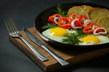 Fried eggs with potato pancakes and herbs in a pan on a black background. Homemade food.