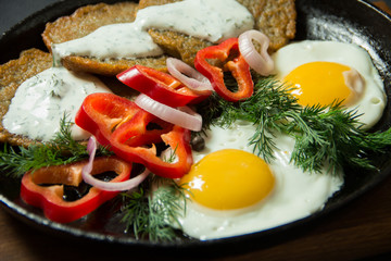 Fried eggs with potato pancakes and herbs in a pan on a black background. Homemade food.