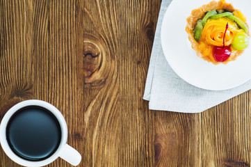 Appetizing cake basket with sliced fruit, berries and cup of coffee, on rustic wooden background with copy space. Delicious and fresh dessert and coffee, top view, flat lay.  Morning choice.
