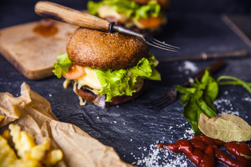 Fast food on the table: burger with beef or pork, or chicken and vegetables, French fries with tomato sauce, basil leaves