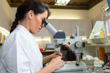 Technician in dental lab working on an implant under microscope