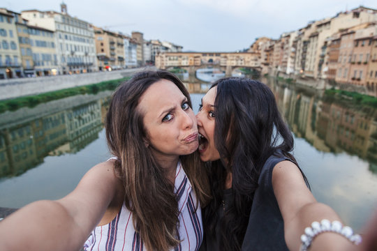 Two beautiful young women friends take selfie at sunset in front of Ponte Vecchio, Florence