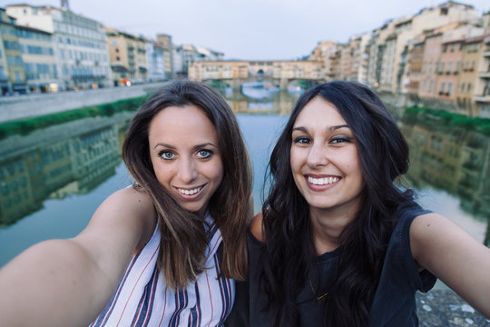 Two beautiful young women friends take selfie at sunset in front of Ponte Vecchio, Florence