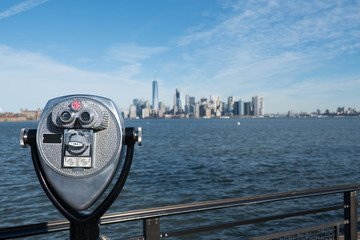 Tower viewer telescope looking at lower Manhattan skyline from Liberty Island. Railing and binoculars on a stand for tourists to view New York City from across the New York Harbor.