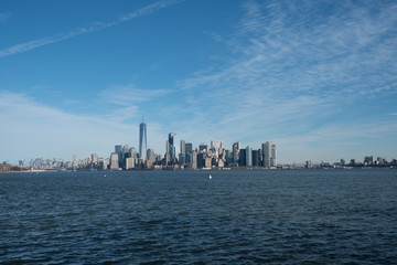 View of lower Manhattan skyline from a ferry.Blue skies and wispy clouds over New York City's Financial district. Tall New York City skyscrapers and New York harbor.